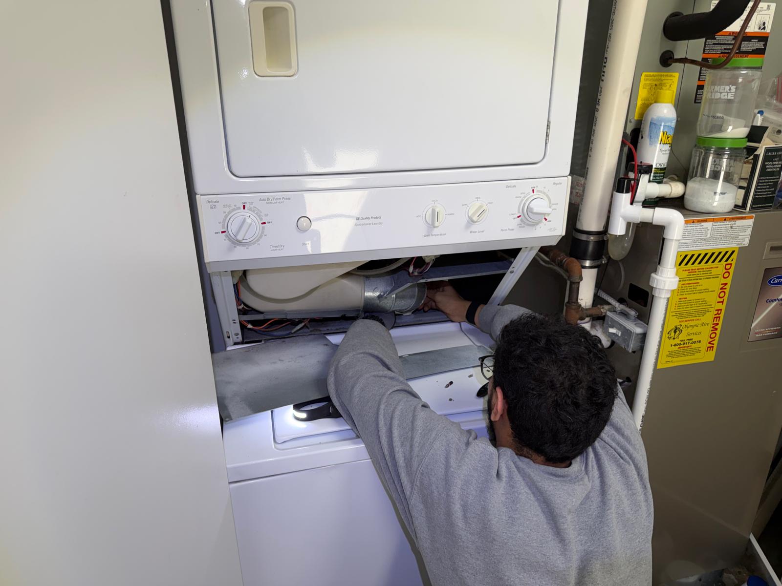 Technician with a headlamp inspecting the control panel of a stacked dryer unit
