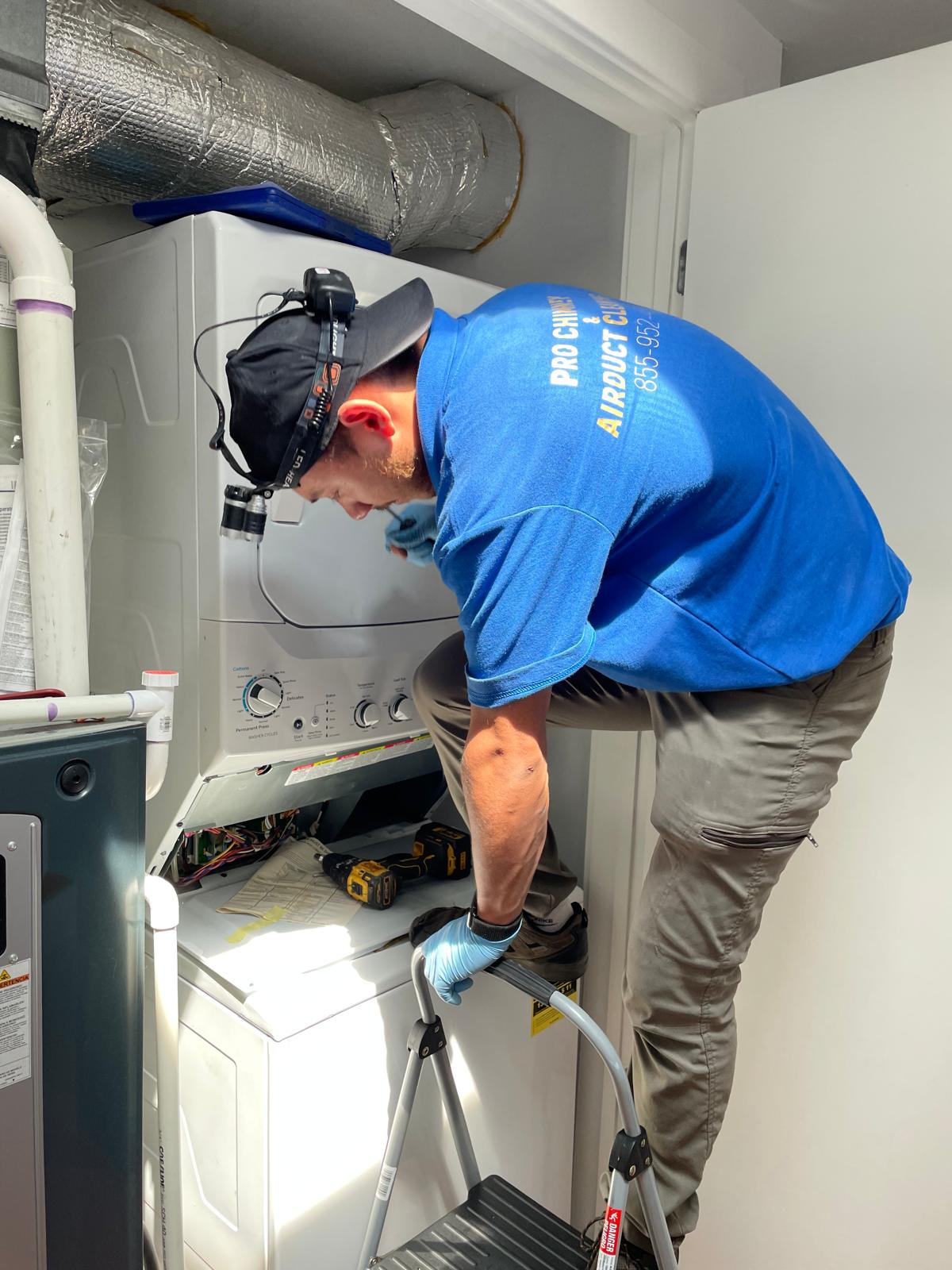 Technician removing the front panel of a GE stacked dryer to begin a repair