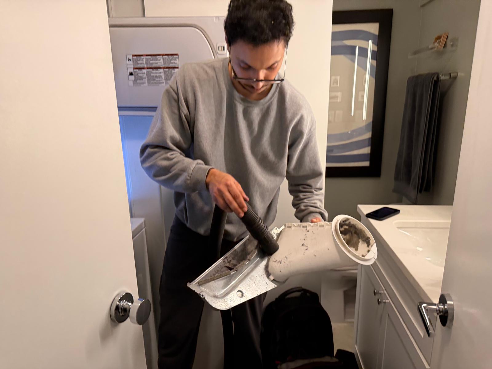 Technician vacuuming lint from a dryer blower housing during a cleaning service