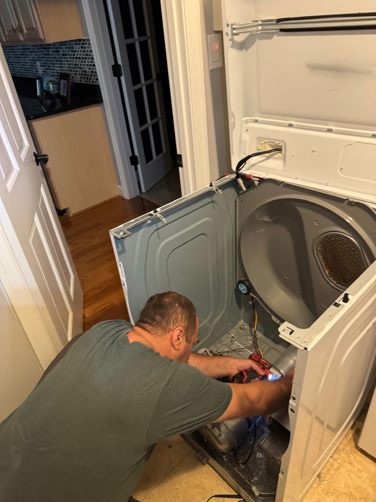 Appliance technician removing the rear panel of an electric dryer with a power drill