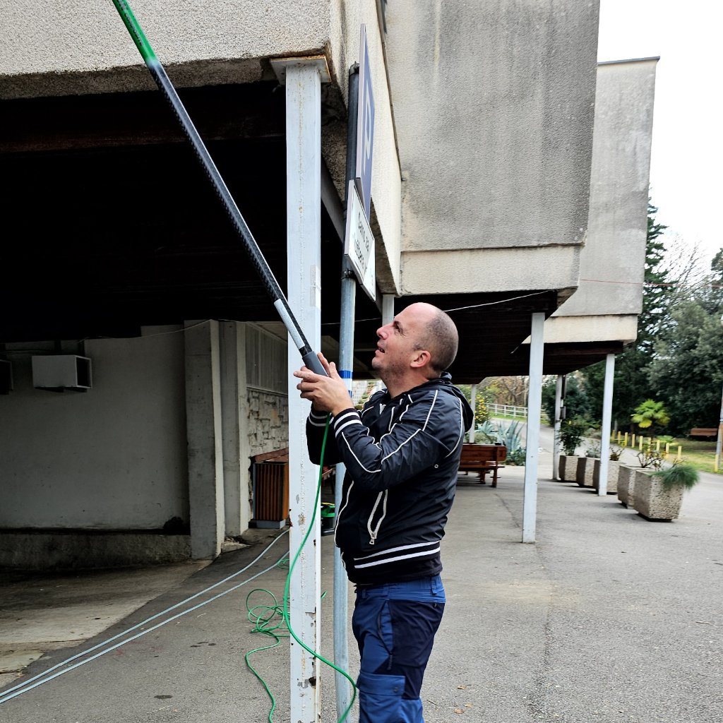 Radnik čisti vanjsku fasadu zgrade telescopskom motkom