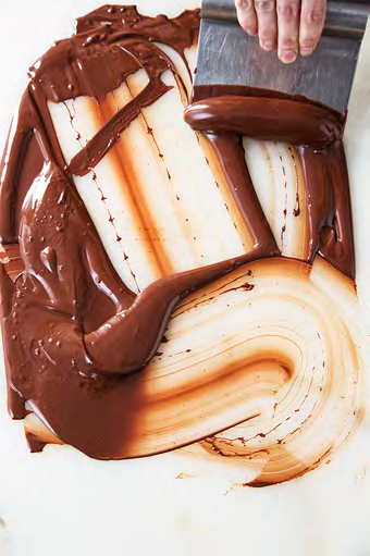 Chocolate being spread and tempered with a steel blade on a stone slab
