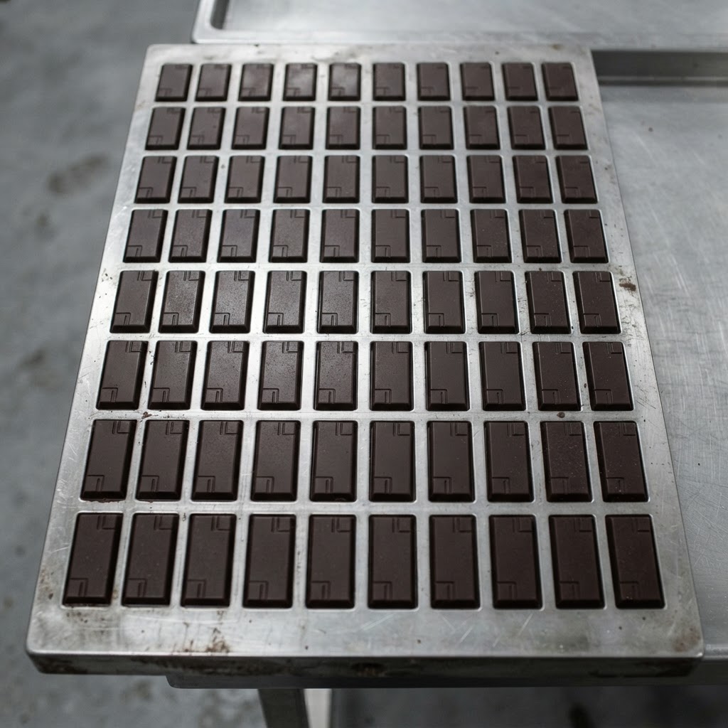 Dozens of identical moulded dark chocolate bars in a stainless steel mould tray