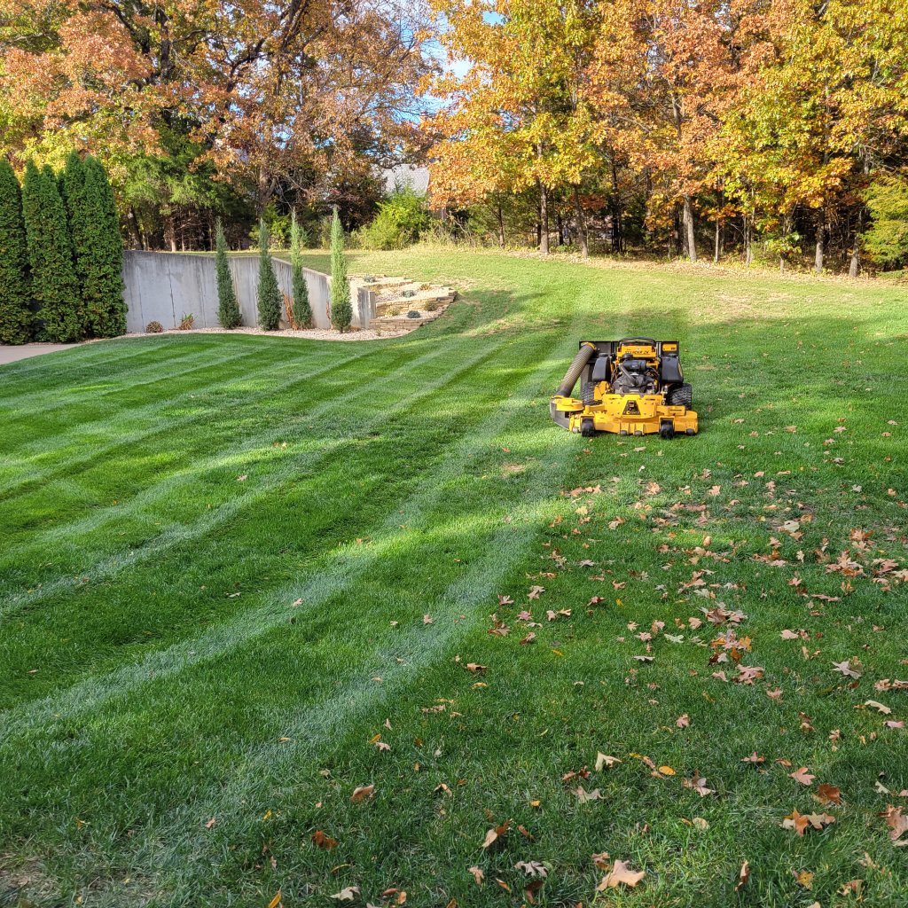 Zero-turn mower on striped lawn with autumn foliage