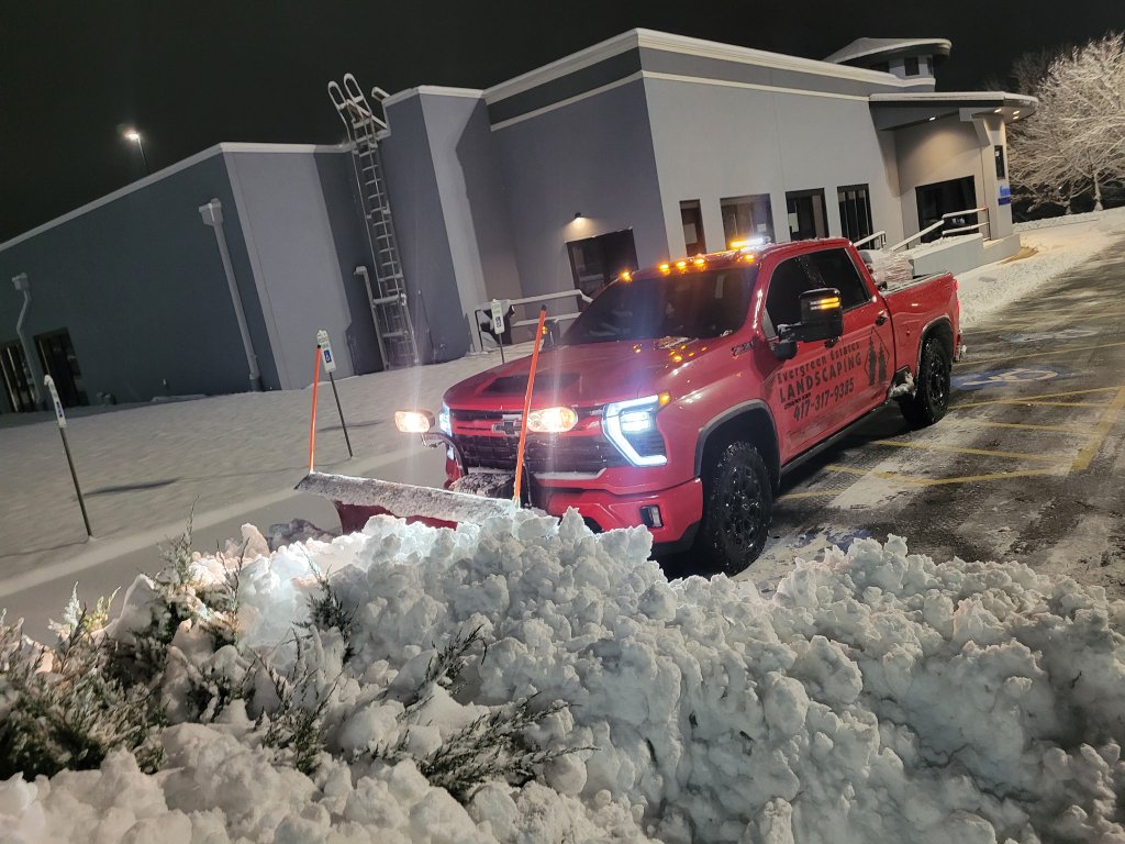 Snow plow truck clearing snow from a commercial parking lot at night