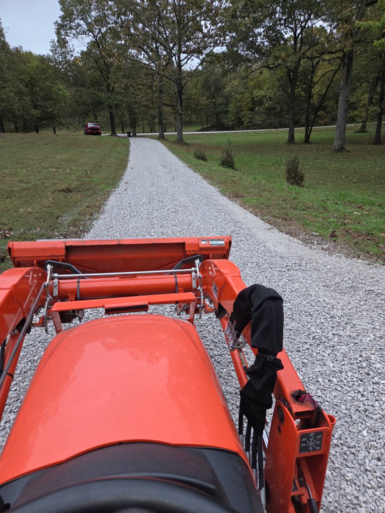 Orange tractor with loader on gravel driveway surrounded by trees