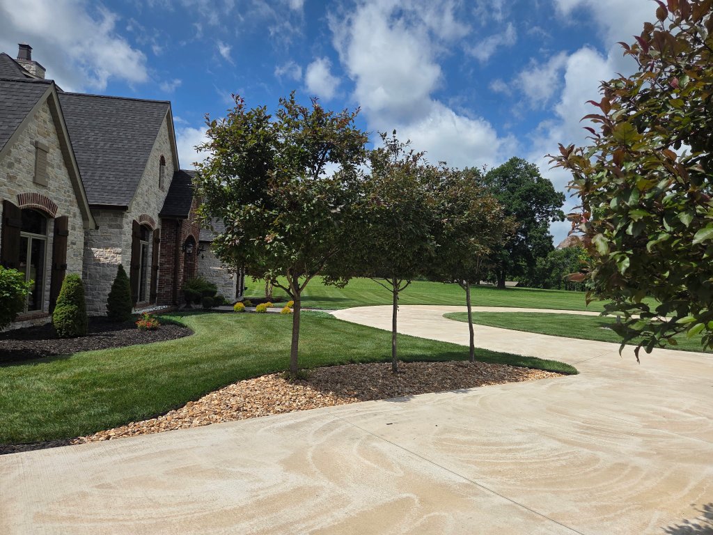 Stone and brick estate with ornamental trees in mulch beds along winding driveway