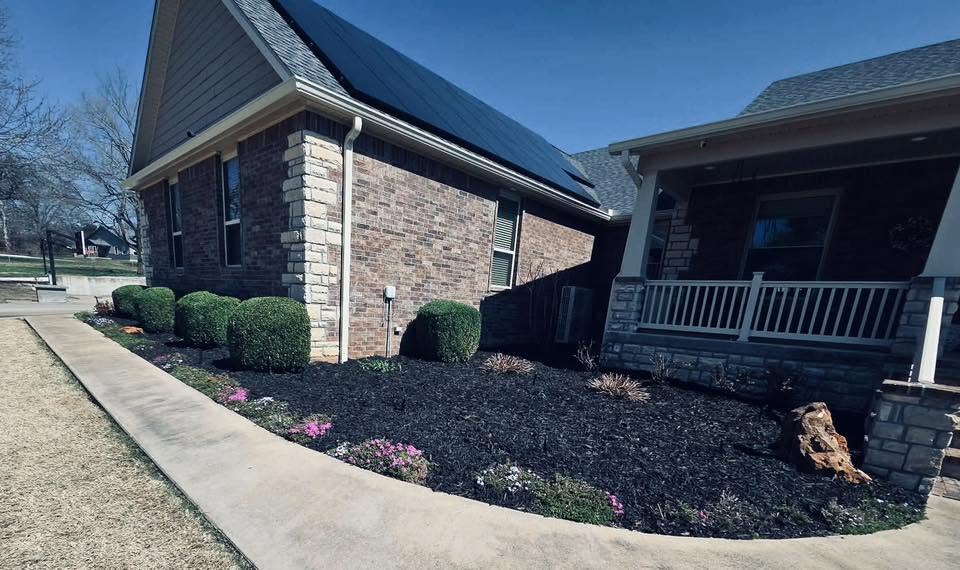 Brick home landscape bed with round shrubs and stone edging