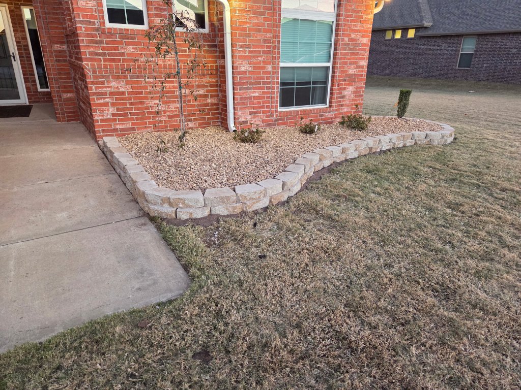 Curved retaining wall with tan blocks and decorative gravel bed in front of brick home