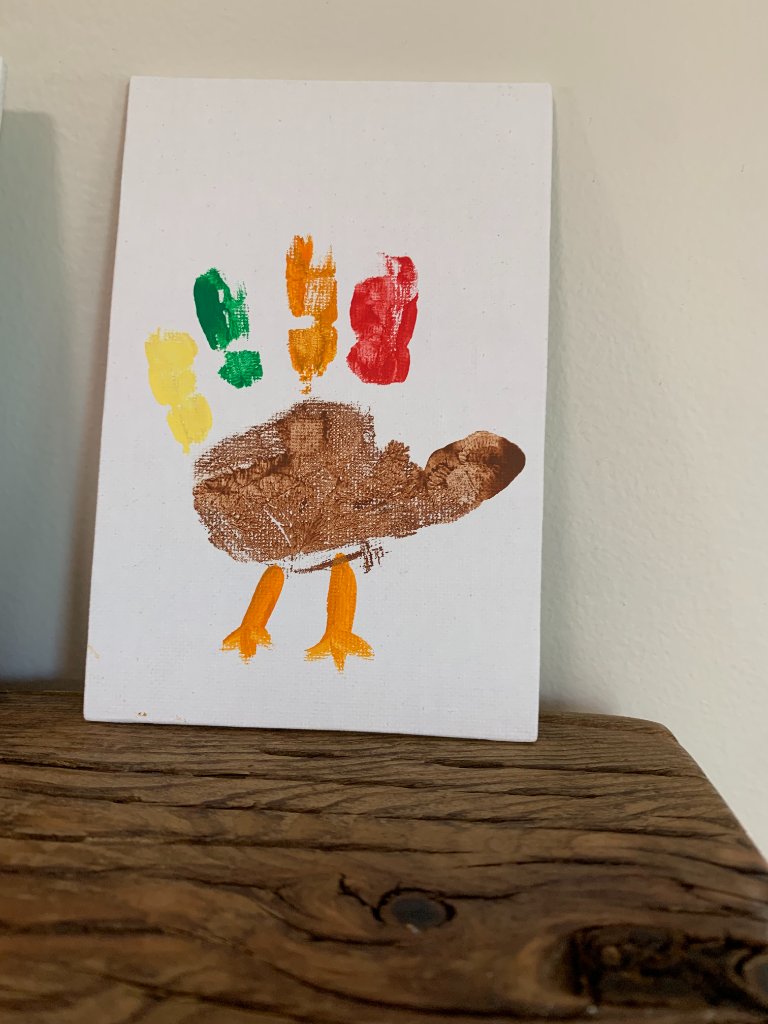 Handprint turkey craft on a small white canvas with colorful finger-paint feathers