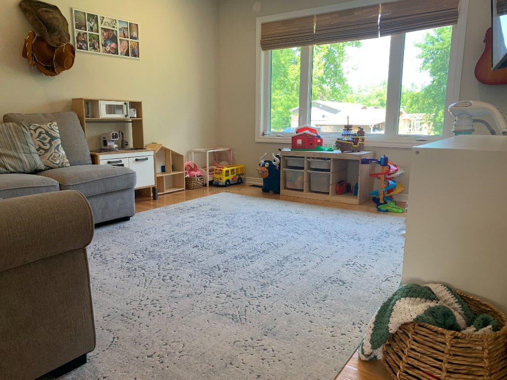 Wide view of the playroom with sofa, play kitchen, dollhouse, and toy shelving unit