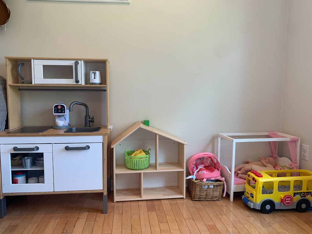 Wooden play kitchen, dollhouse, and doll bed with toy school bus in the daycare playroom