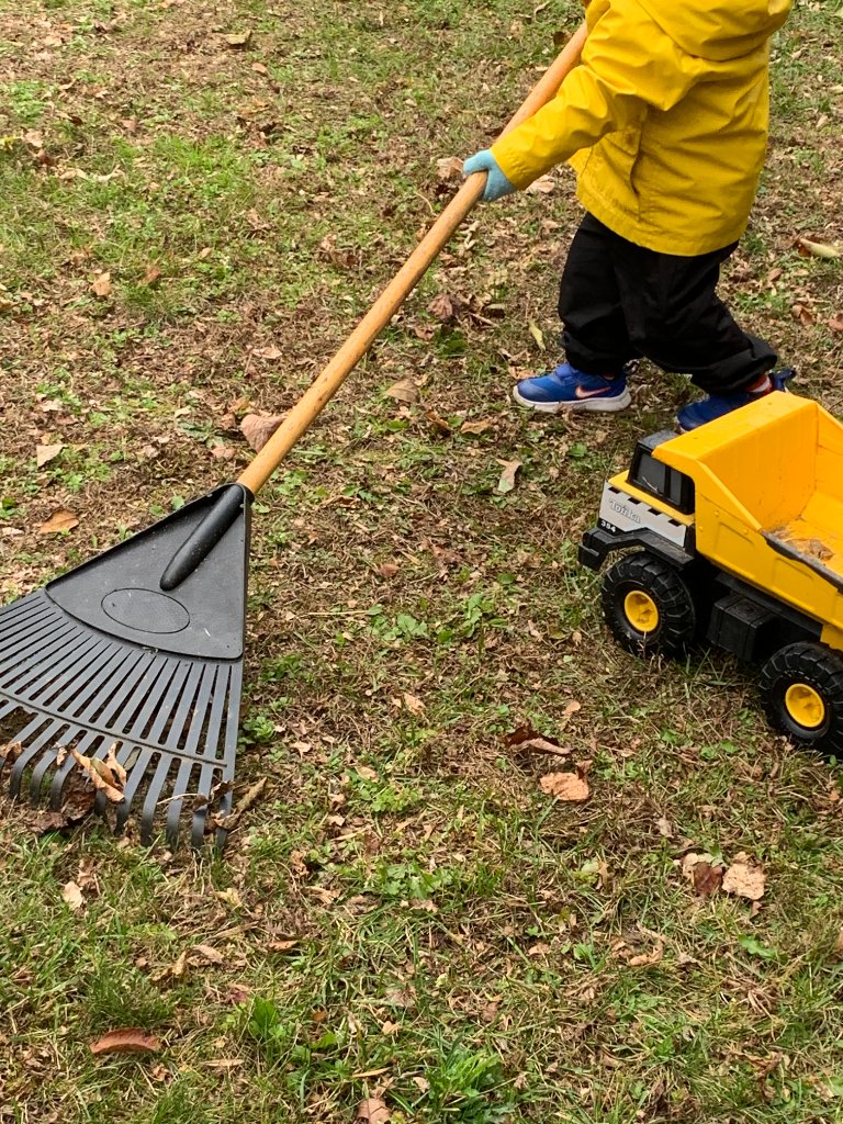 Child in yellow rain jacket raking autumn leaves with a Tonka dump truck nearby
