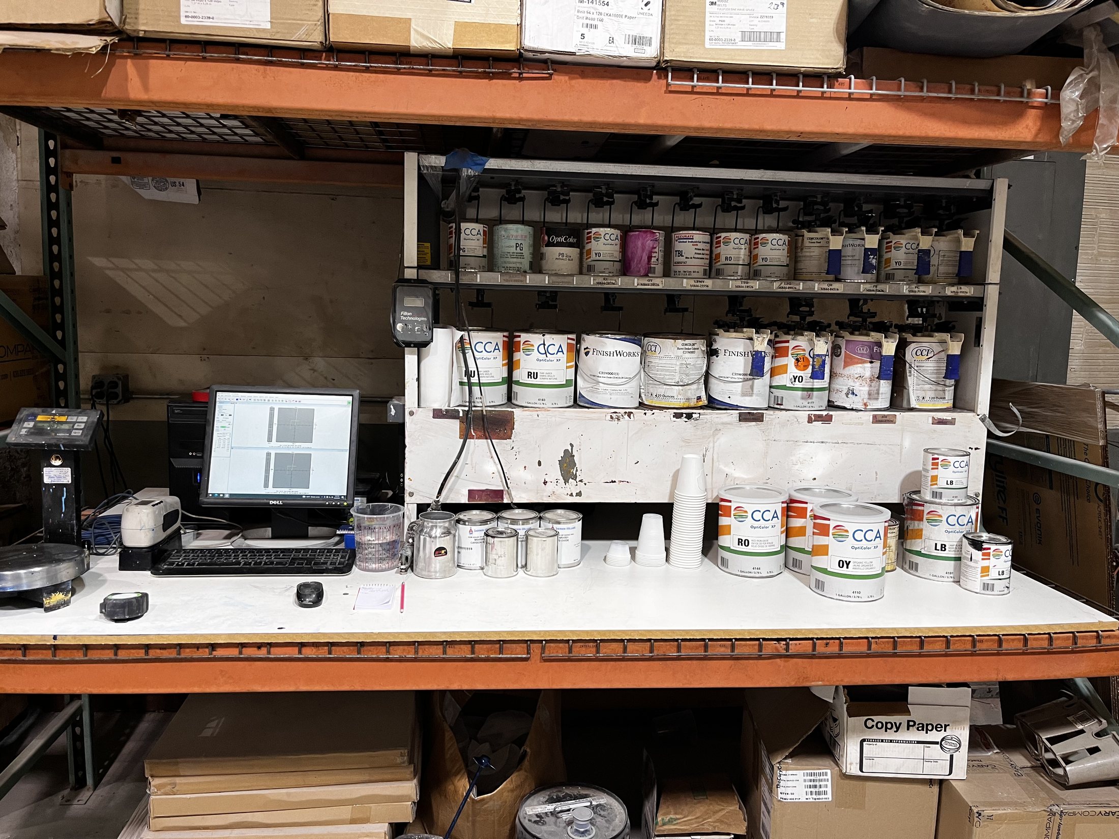 A color-mixing workbench with a monitor, scales, and labeled cans.