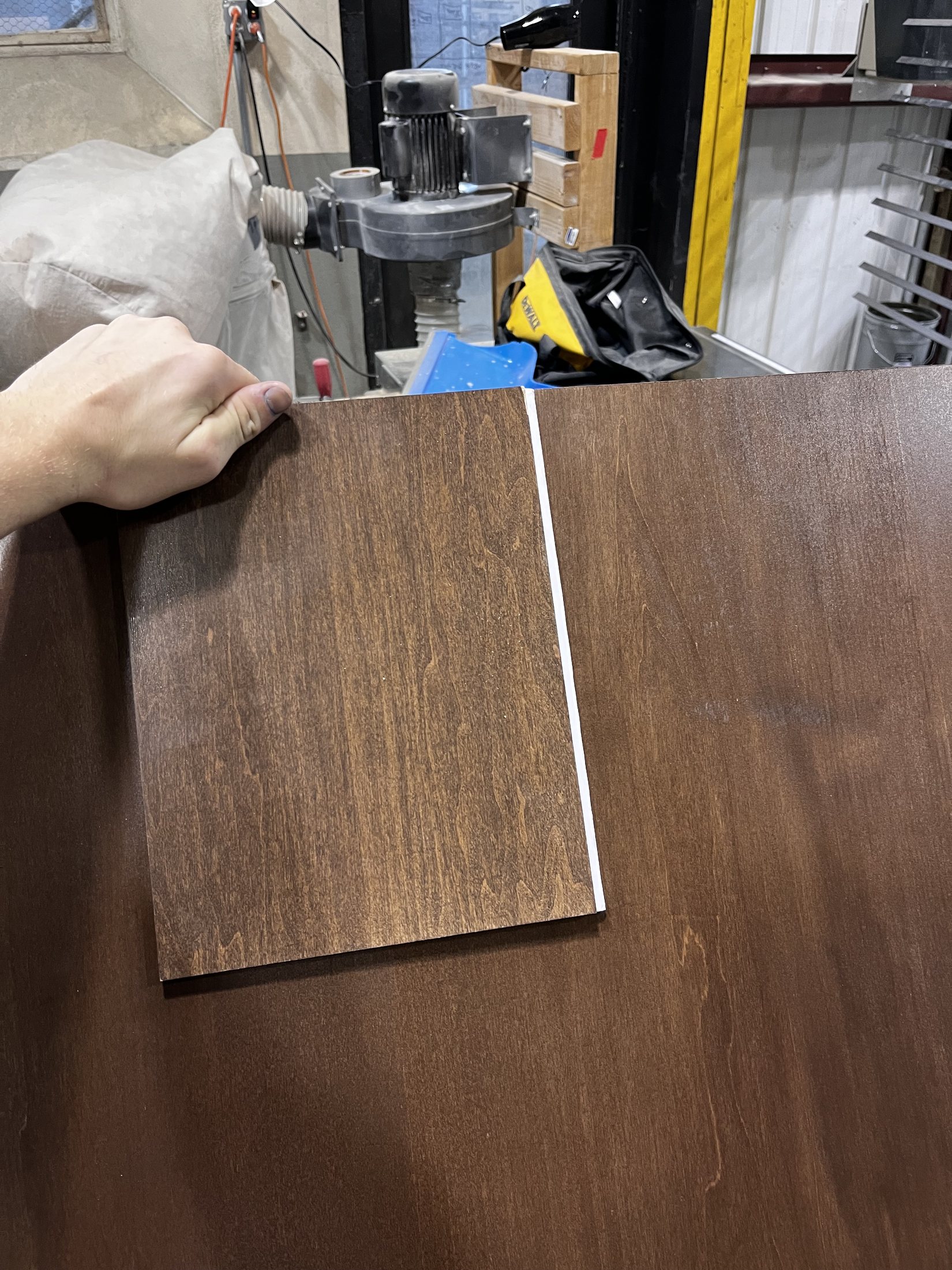 A hand holding a dark wood veneer sample over a lighter base panel.