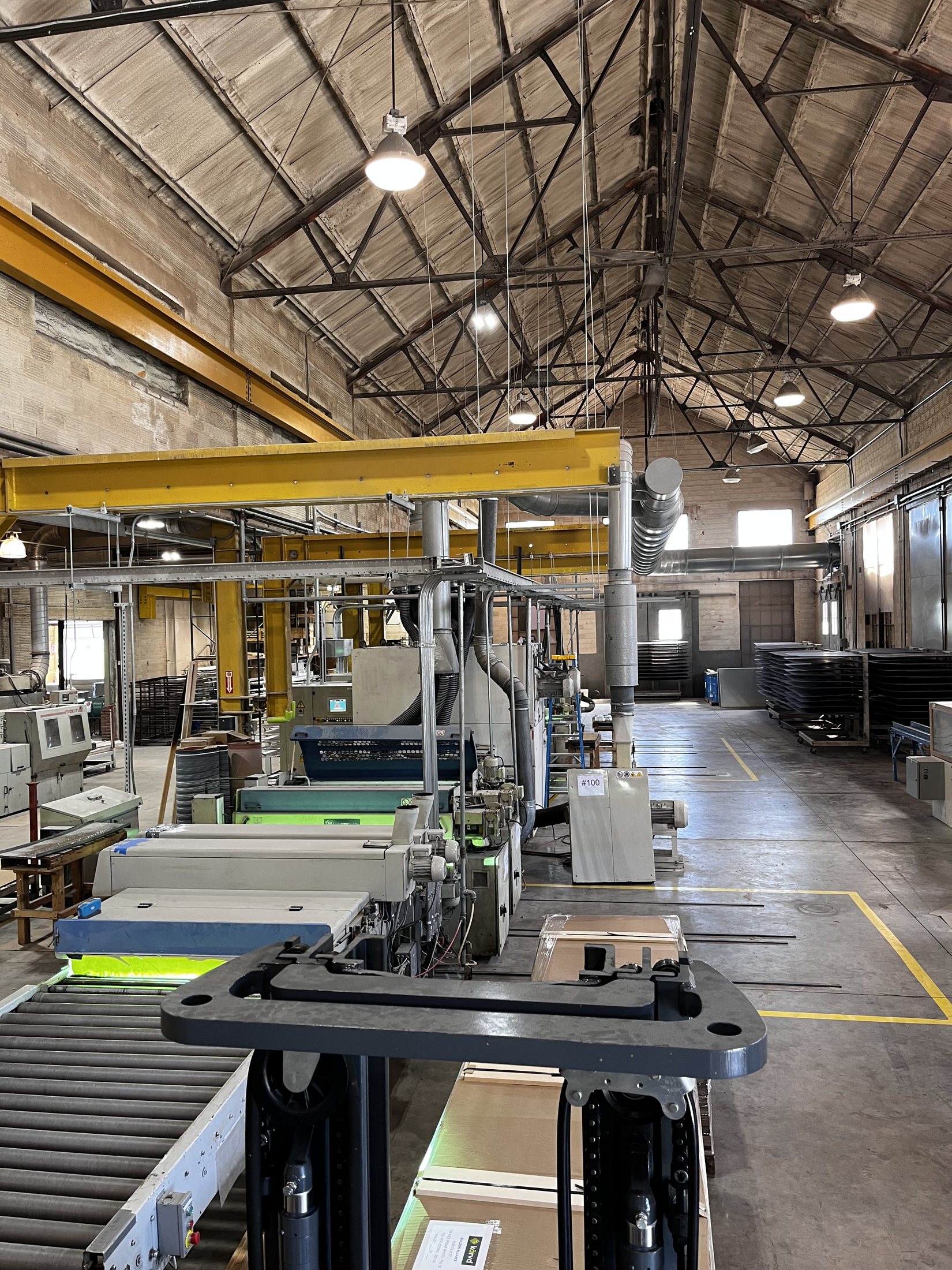 Portrait view of a manufacturing floor showing assembly machinery and an overhead crane beam.