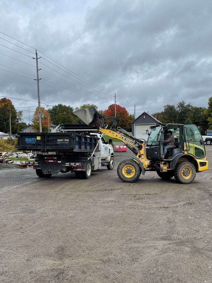 Yellow loader filling a black BAM truck bed on a job site