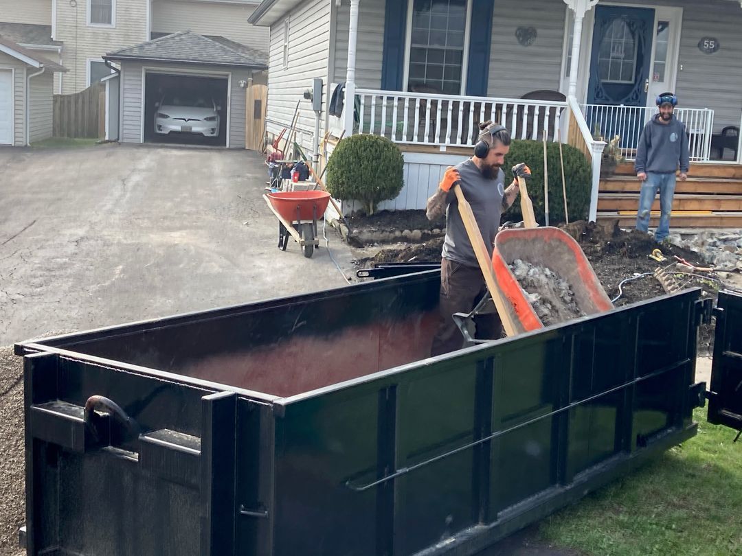 Crew loading debris into a bin with shovel and wheelbarrow during a cleanout