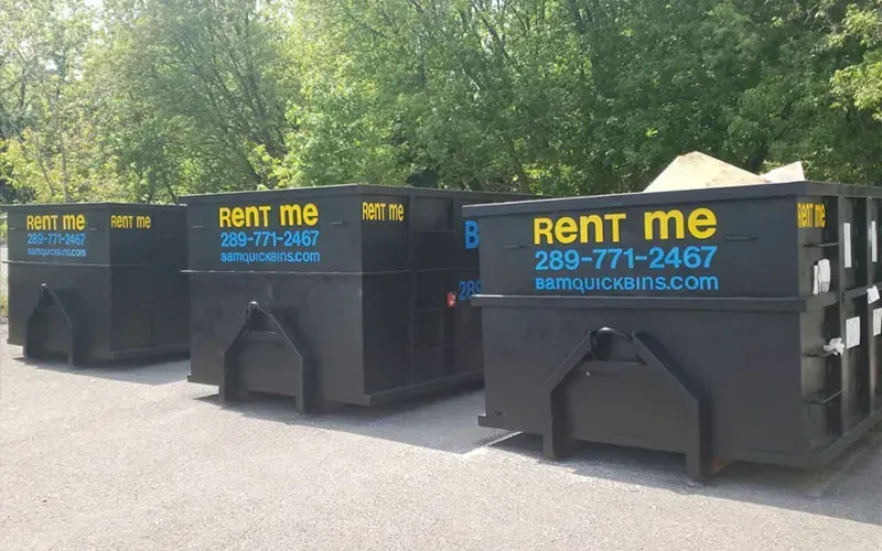 Three black BAM roll-off bins with 'Rent Me' signage lined up