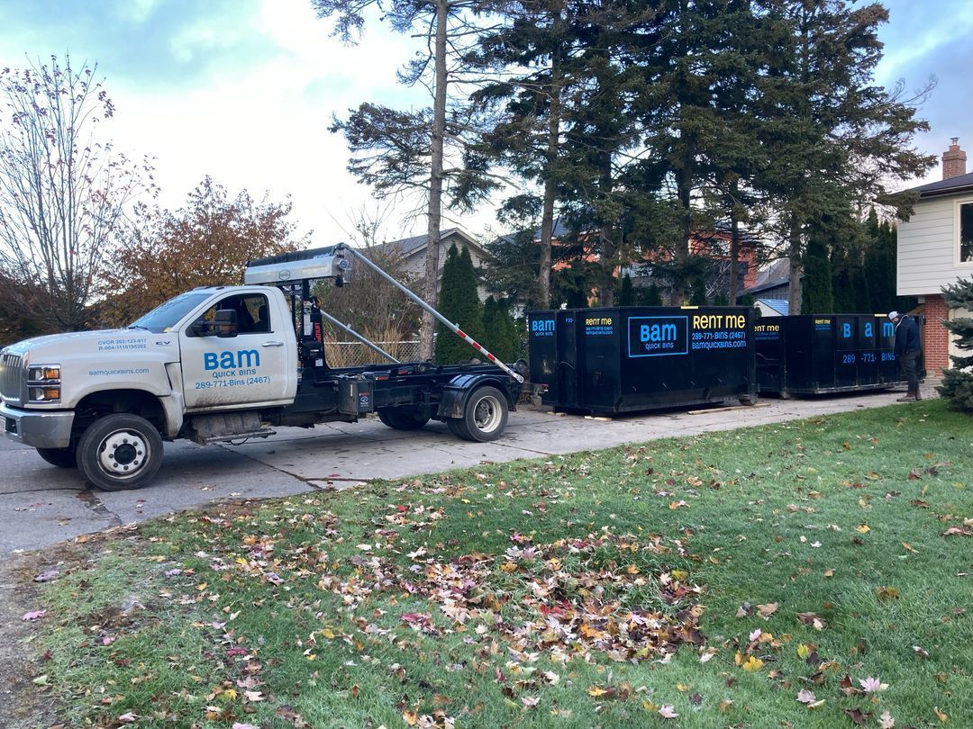 White BAM truck delivering a roll-off bin on a residential driveway