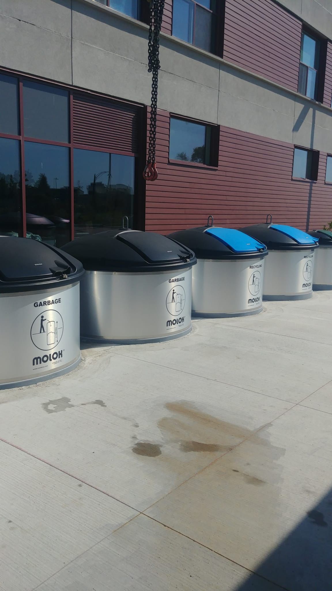 Row of Molok semi in-ground garbage and recycling bins beside a building during a crane servicing visit