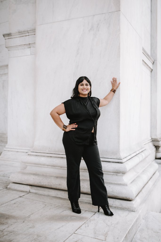 Revathi leaning against a marble pillar in all-black attire
