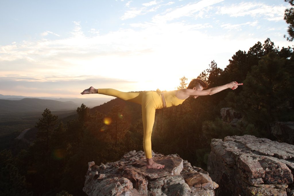 Nicole Warren in Warrior III pose on a Sedona cliffside at sunset