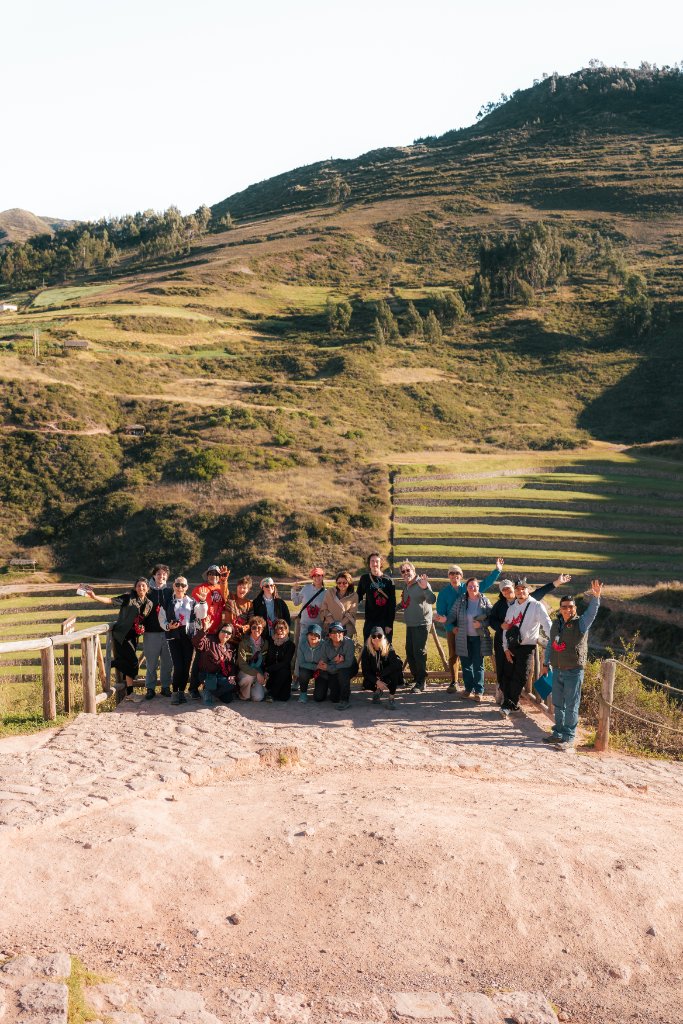 Vivara retreat group posing together at the Maras Salt Mines in the Sacred Valley of Peru, with terraced salt pans and Andean mountains behind them