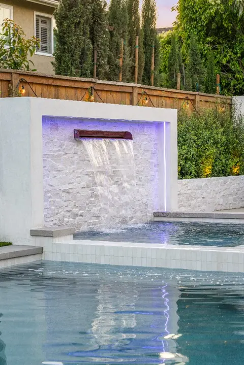 Gas fire pit with stone seat wall beside a custom pool in Huntington Beach, California