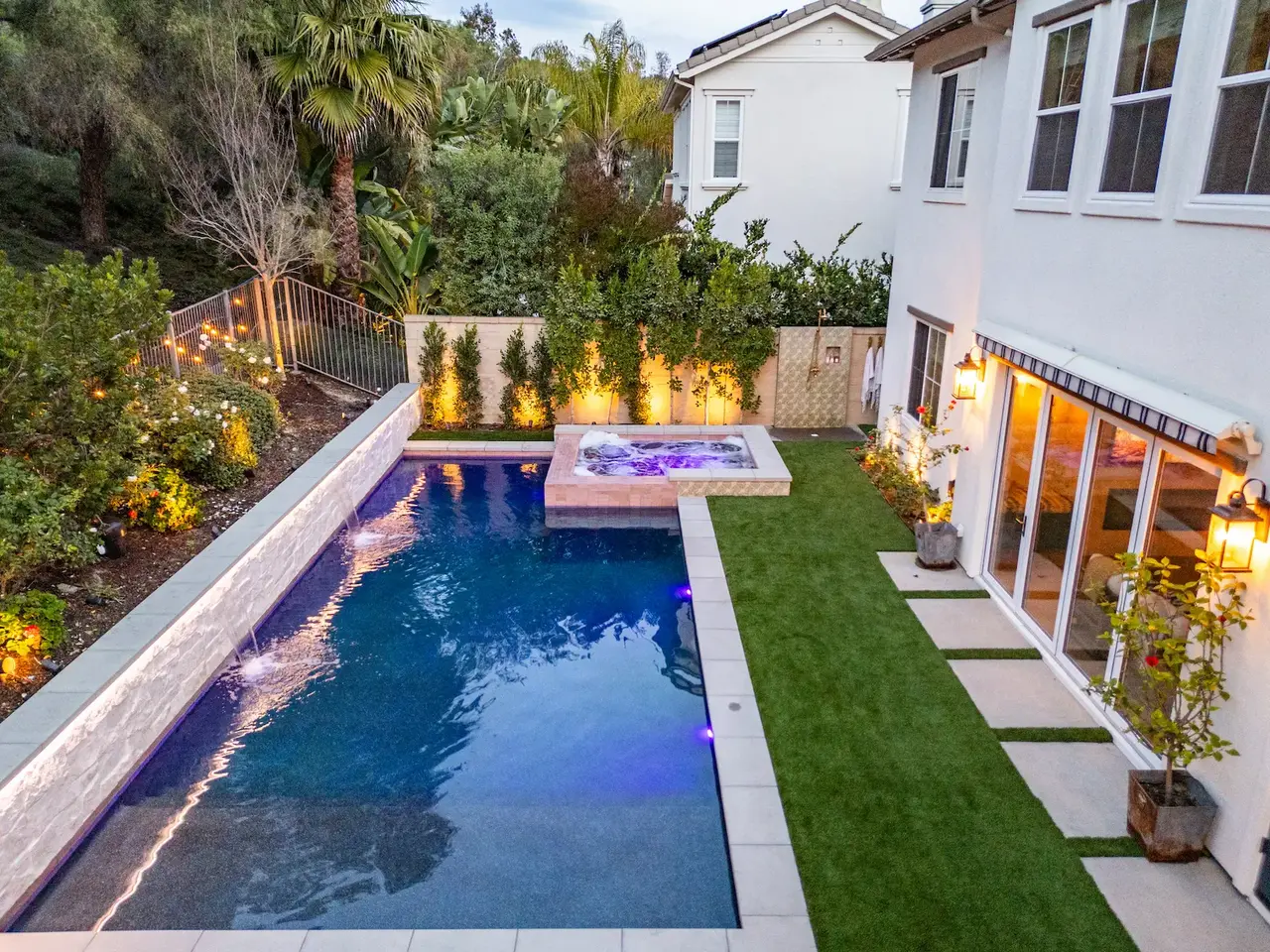 Twilight view of a custom pool and raised spa with sheer-descent waterfalls in San Clemente, California
