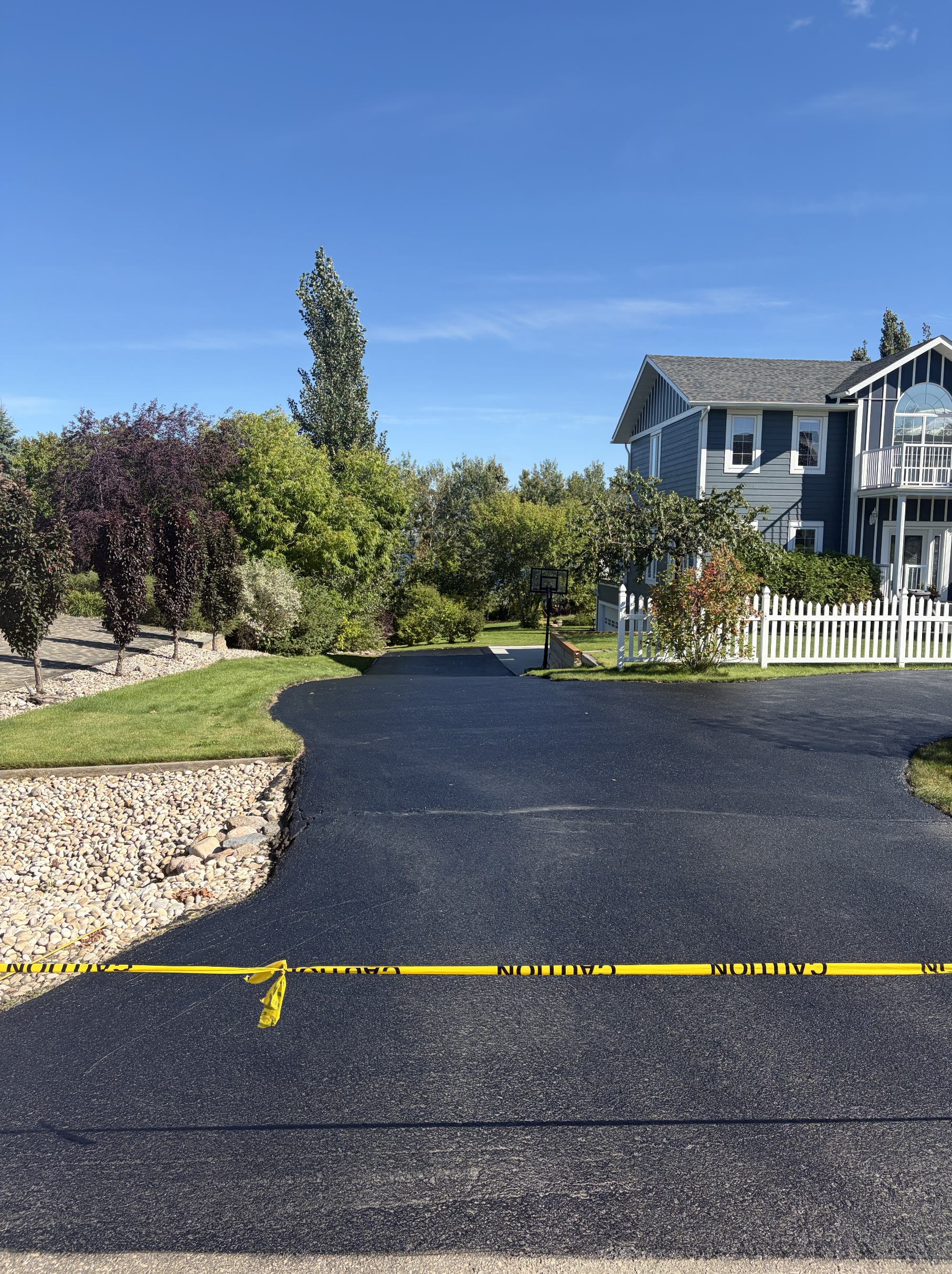 Freshly sealed driveway, curing behind caution tape, after oil-based sealant