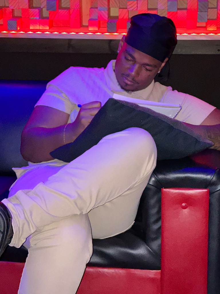 Kobie Alleyne writing lyrics in the studio with a notebook and pen