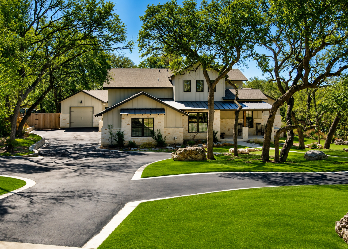 Two-story farmhouse with board-and-batten siding, stone masonry, dark metal awnings, and a tree-lined driveway