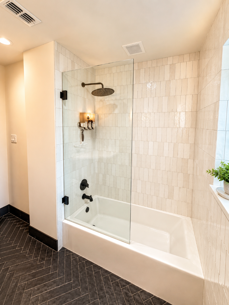 Frameless glass shower with vertical subway tile, matte black fixtures, and herringbone floor