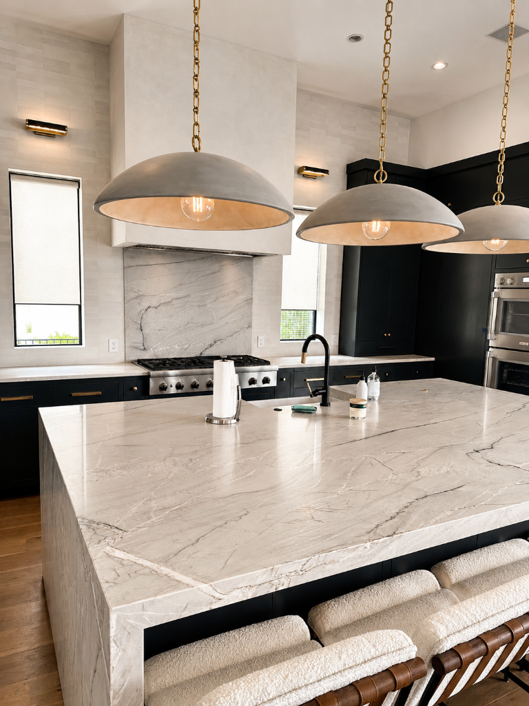Matte black cabinetry with marble waterfall island, plaster range hood, brass dome pendant lights, and bouclé bar stools on light oak flooring