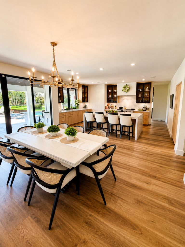 Open-concept kitchen and dining with oak cabinetry, marble island, and brass chandelier over a poolside view