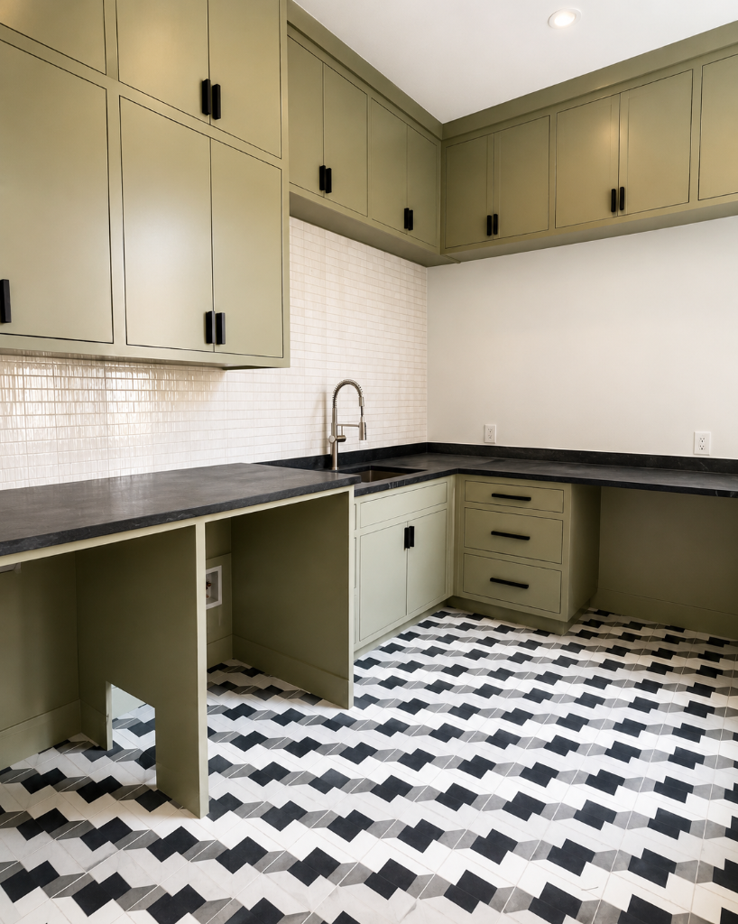 Shaker-style olive green cabinetry with matte black hardware, dark stone countertop, stacked white tile backsplash, and a bold geometric black-and-white patterned tile floor