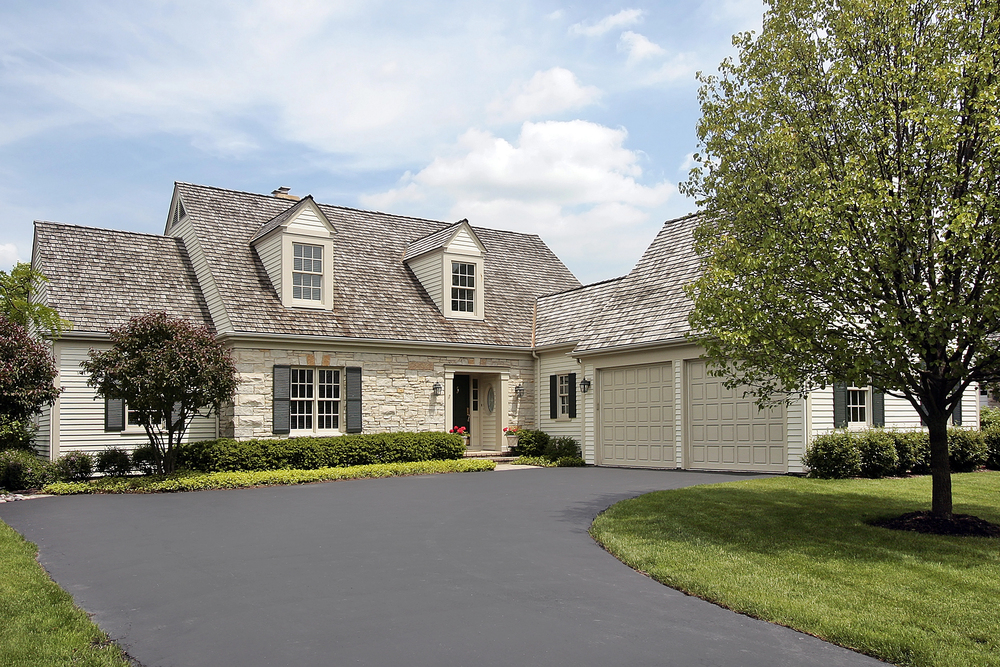 Two-story home with beige siding, stone veneer accent, arched dormers, and two-car garage