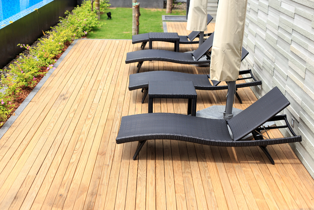 Poolside wooden deck with woven-wicker lounge chairs and beige patio umbrellas