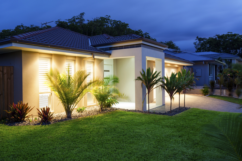 Modern single-story home at dusk with warm interior glow and tropical landscaping