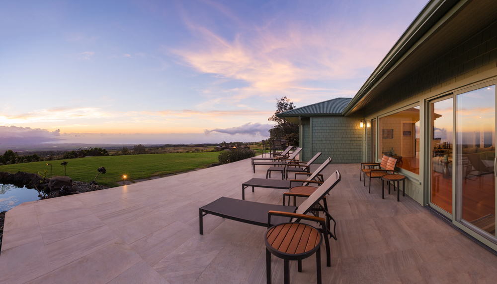 Modern patio at sunset with lounge chairs overlooking rolling hills and water