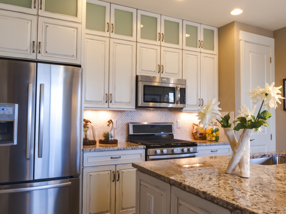 Distressed cream kitchen with glass-front uppers, under-cabinet lighting, and granite island