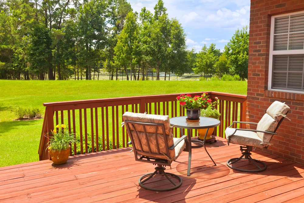Redwood deck overlooking a green lawn and tree line with brick home exterior