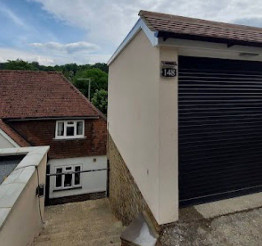 Beige rendered garage with roller shutter door beside residential property