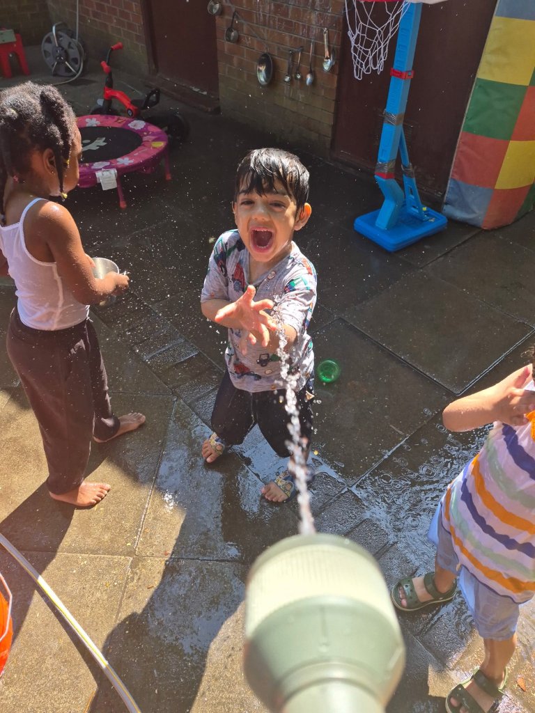Children laughing during outdoor water play in the garden at Morning Glory Pre-School