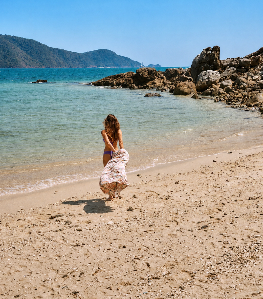 A woman walking toward turquoise water on a sandy beach in Phuket
