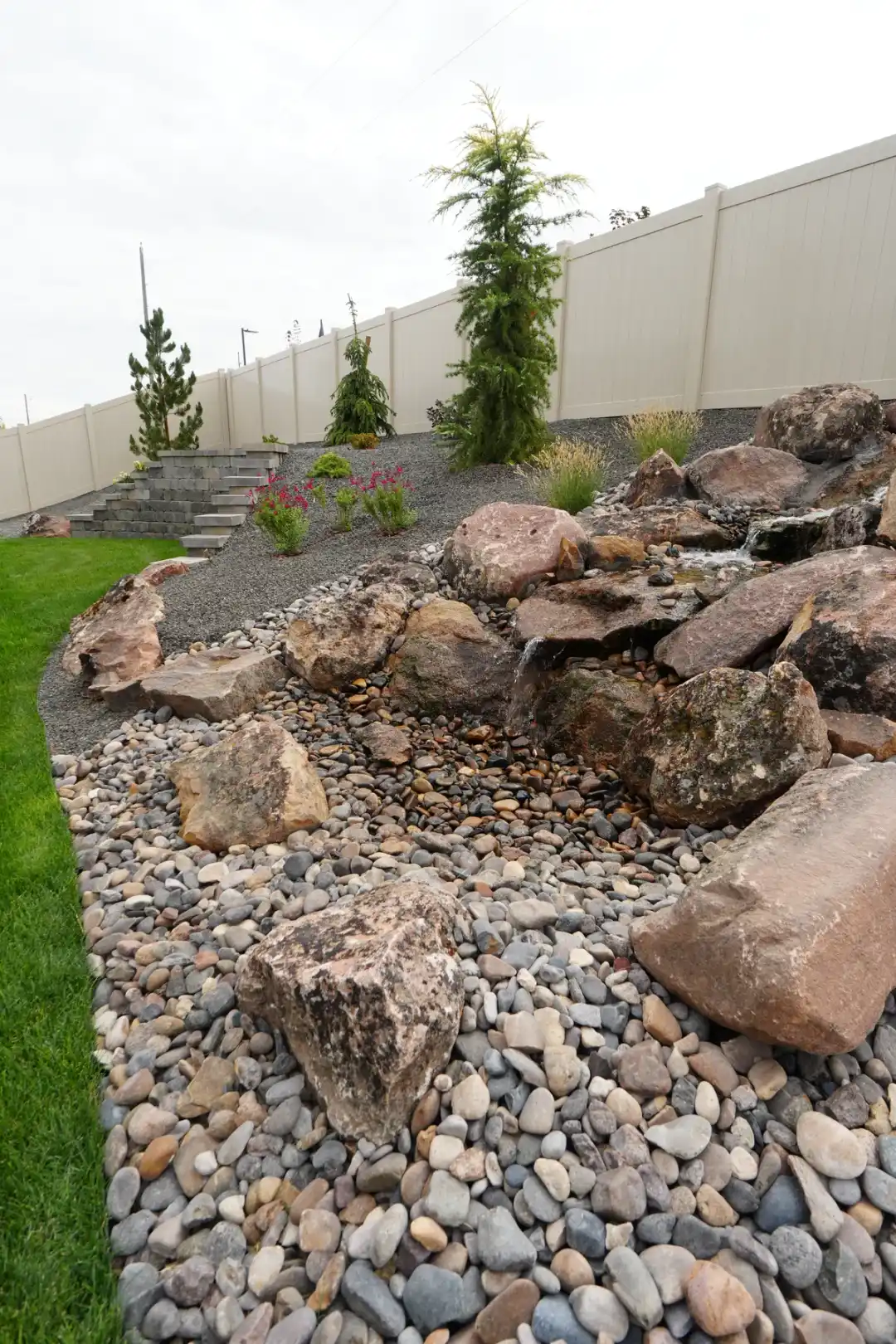 Natural boulder water feature with river stone bed, retaining wall, and plantings