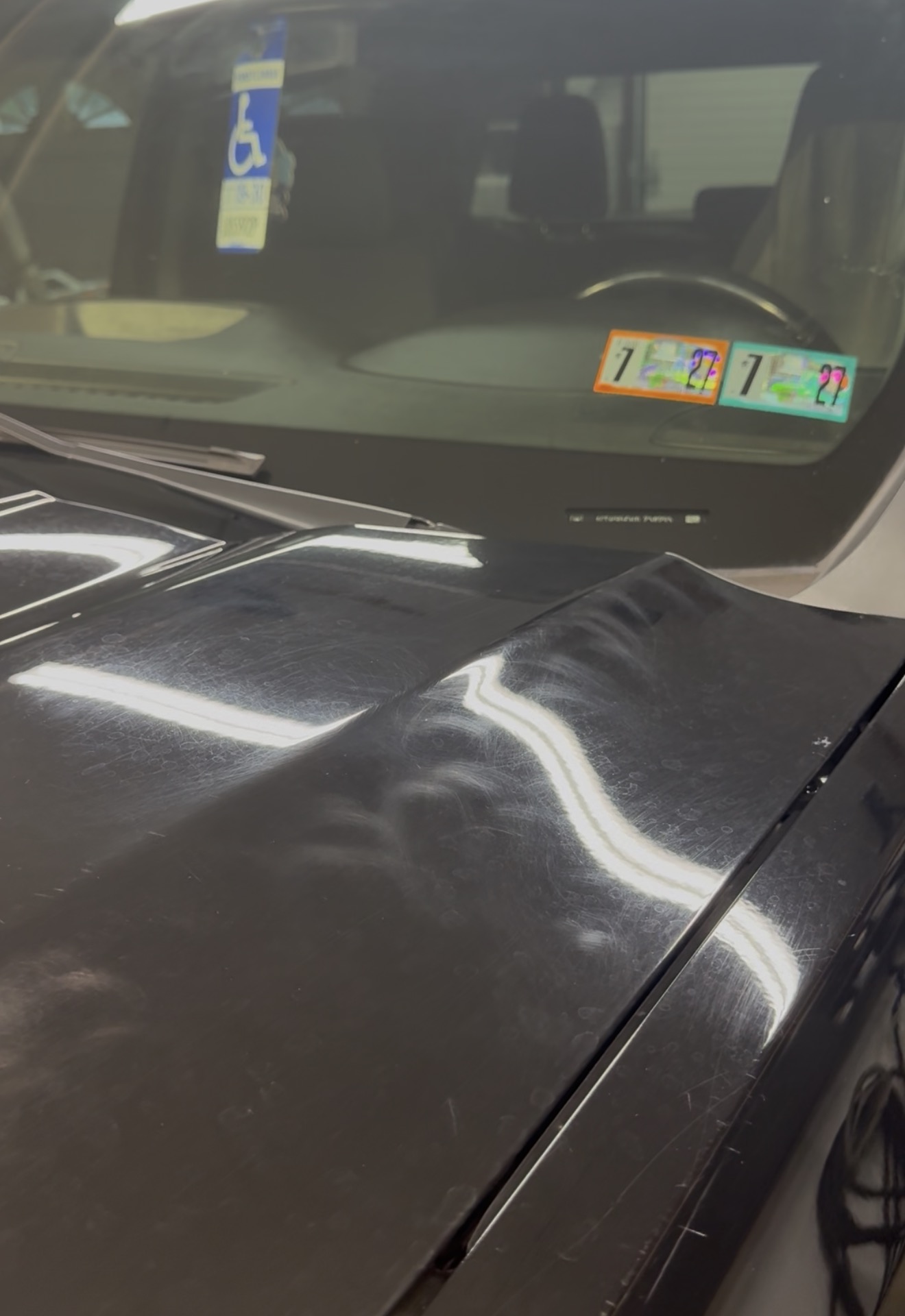 Black vehicle hood covered in heavy swirl marks and fine scratches before paint correction