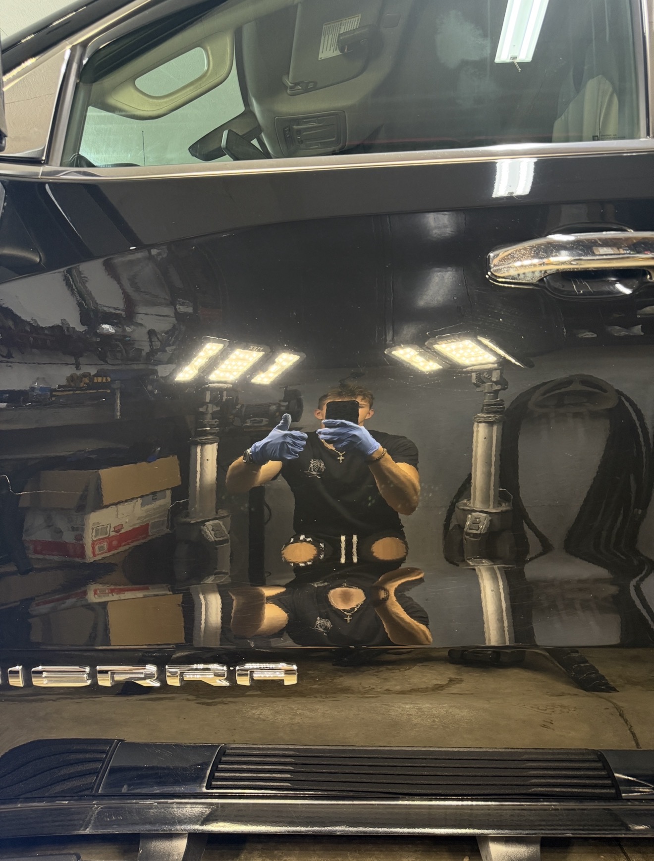 Selfie reflected in the polished black door panel of a GMC Sierra under LED studio lighting