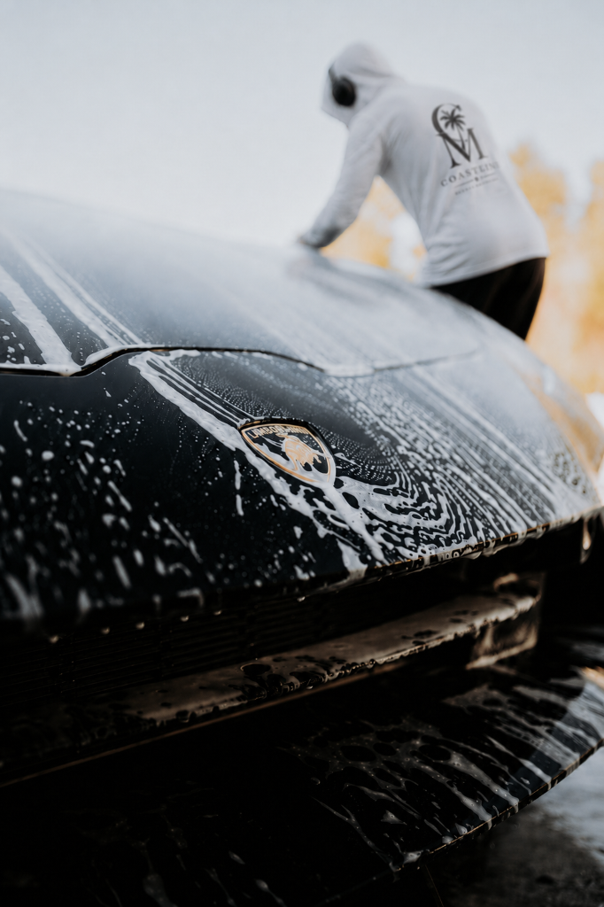 Coastline Mobile Detailing technician washing a black Lamborghini covered in soap suds